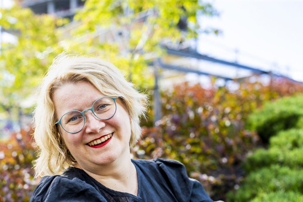 Jenni Gästgivar seisoo talon pihalla ja hymyilee kameralle